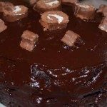 Glossy chocolate cake with small flakes and chocolate rolls on top