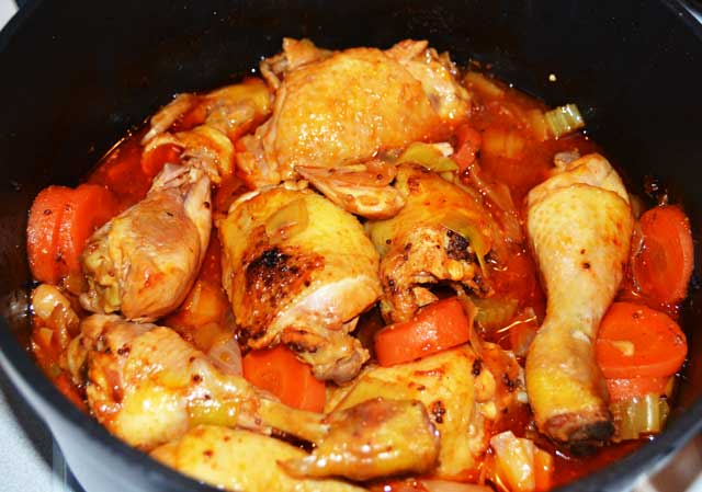 Chicken thighs and chicken drumsticks cooking in a casserole with vegetables