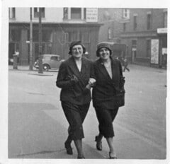 two 1920s ladies walking down the street arm in arm