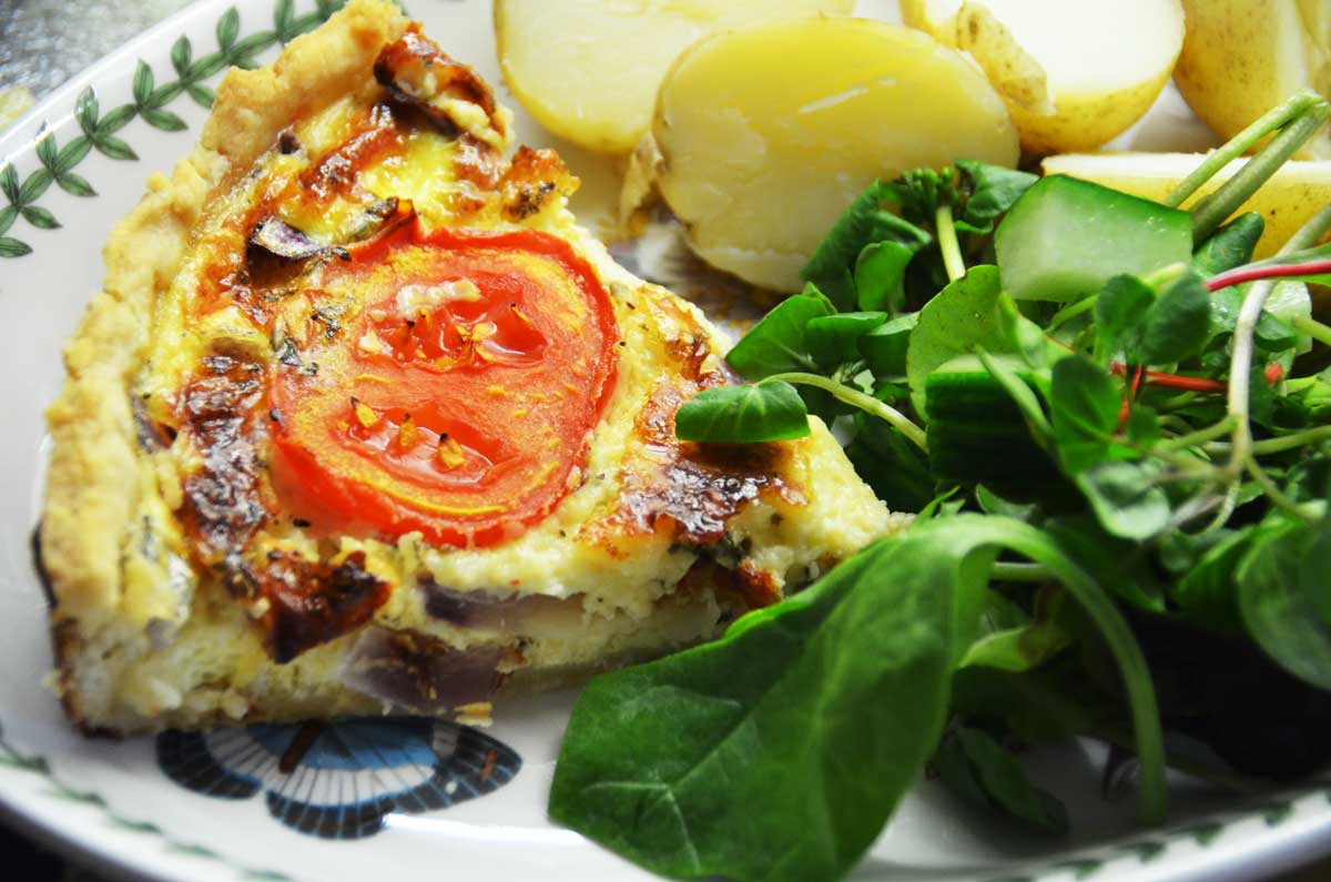 slice of cheese and tomato quiche served with new potatoes and green salad leaves