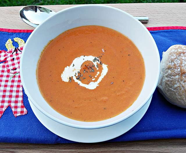 Cream of Tomato and basil soup in a bowl with spoon and roll