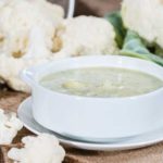 bowl of cream coloured soup with cauliflower florets next to it