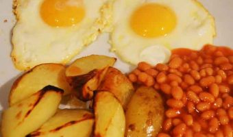 two fried eggs with potato wedges and beans on a plate