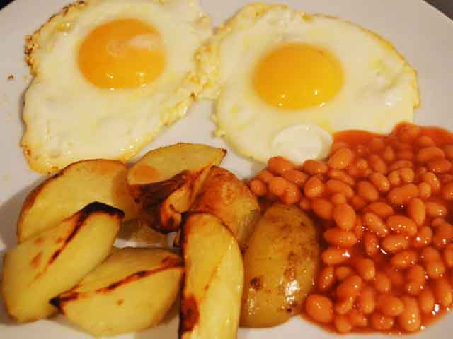 two fried eggs with potato wedges and beans on a plate