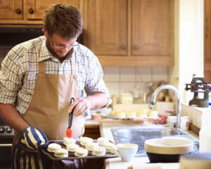 man wearing apron with small cakes and a pastry brush