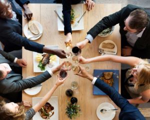 looking down on six people raising a glass to each other after a meal