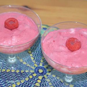 two pink desserts in glass stem bowls with raspberry in middle