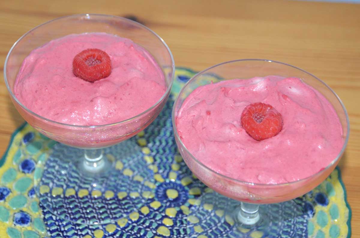 two pink desserts in glass stem bowls with raspberry in middle