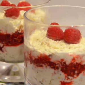 dessert with layers of cream and raspberries and whole raspberry on top in whisky glass