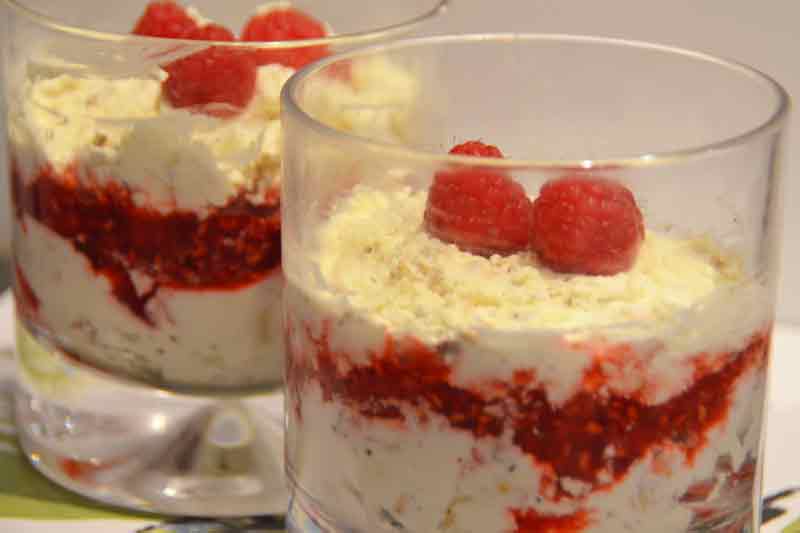 dessert with layers of cream and raspberries and whole raspberry on top in whisky glass