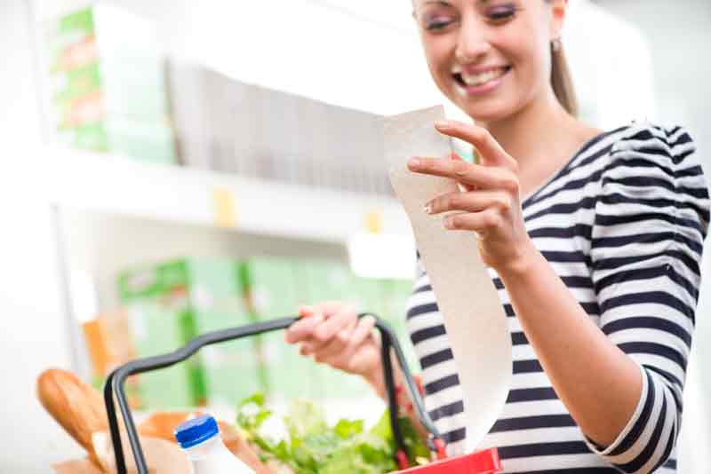 woman with shopping basket looking at till receipt and smiling