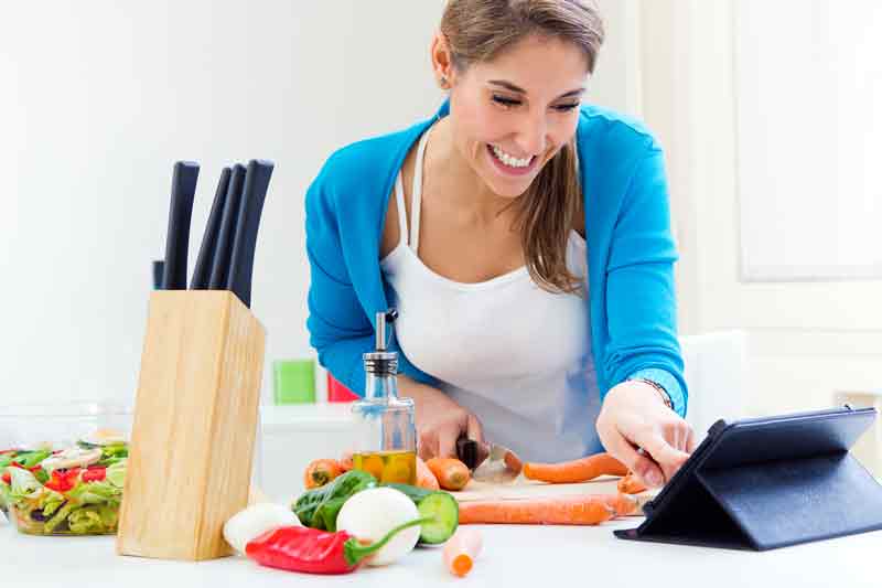 woman looking at tablet whilst cooking in kitchen